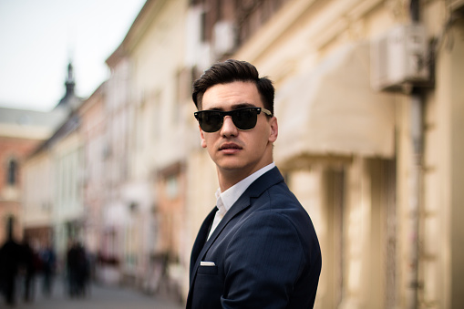 Portrait of a young elegant businessman outdoors on the street in suit and sunglasses.