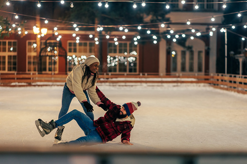 Biracial couple ice skating on a frozen lake. African woman trying to pick up her boyfriend