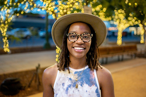 Beautiful African-American Woman in Her Twenties Wearing a Hat in a Park in El Paso Texas Under Decorative Lighting Interacting on a Laptop on a Conference Call