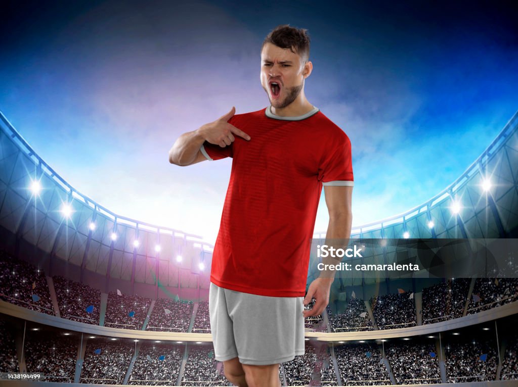 Soccer player with the uniform of his country on stadium. Professional soccer player in Switzerland national team jersey with ball in hands staring with challenging expression on Stadium full of public in the background. 2022 Stock Photo