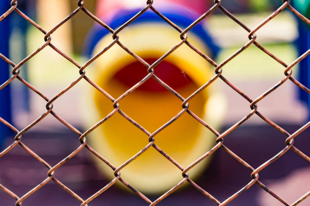 Old corroded chain link fence with a tube slider of a kindergarten yard in the background