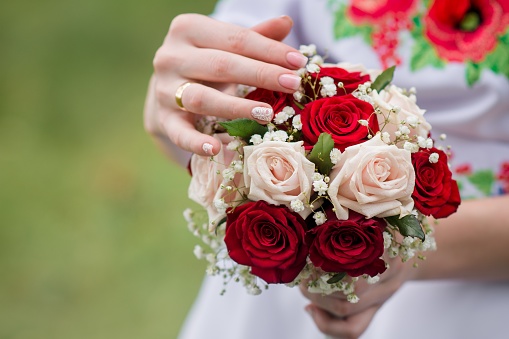 Wedding bouquet with red and pink roses. The girl's hand touches the flower petals in her bouquet. Selective focus