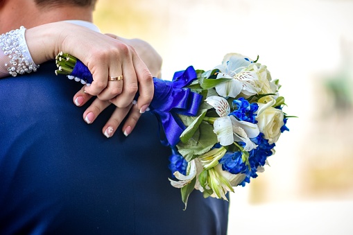 A wedding bouquet in white and blue tones in the hands of the bride, she hugs the groom. Selective focus. With free space for labels