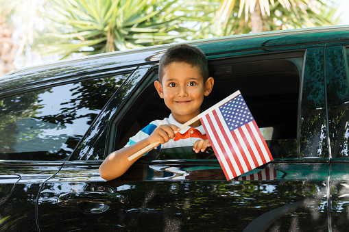 Boy in car is holding American flag with a cute smile.