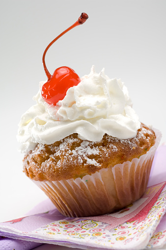 Vanilla muffins in paper baking cup toppled with whipped cream.