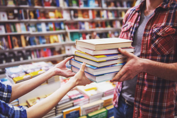 Young people at the book shop Cropped image of young man and woman holding a pile of books while standing in the book shop bookstore stock pictures, royalty-free photos & images