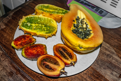Cut halves of exotic fruits lie on a white plate. Ripe horned melon, papaw, tamamoro and pear cactus close-up