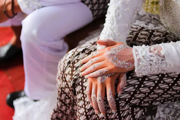 Photo of Traditional Sundanese Bride with white nail art and white kebaya dress sitting beside her husband on the wedding aisle