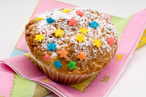 Vanilla muffin in paper baking cup toppled with colorful sprinkles .