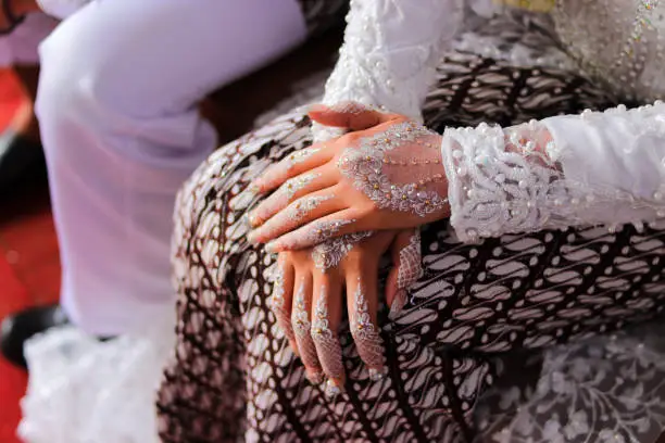 Photo of Traditional Sundanese Bride with white nail art and white kebaya dress sitting beside her husband on the wedding aisle