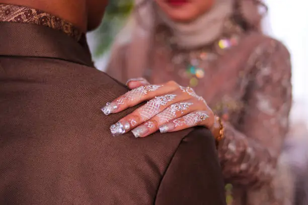 Photo of Asian muslim Bride with white nail art and beautiful hijab holding her husband shoulder