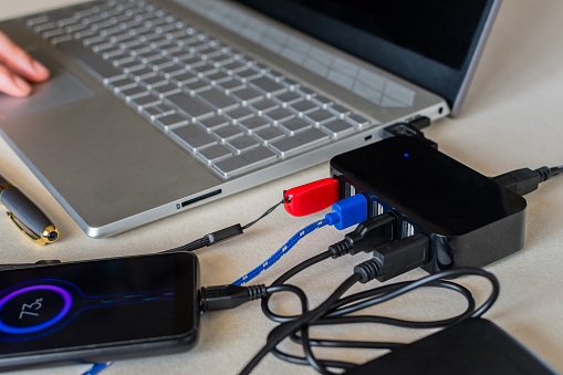 A USB splitter device. Seven port USB next laptop on a desk. Charge cell phone battery. Selective focus.