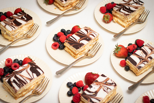 Rows of Napoleon dessert pastries and colorful mixed berries plated with silver forks.