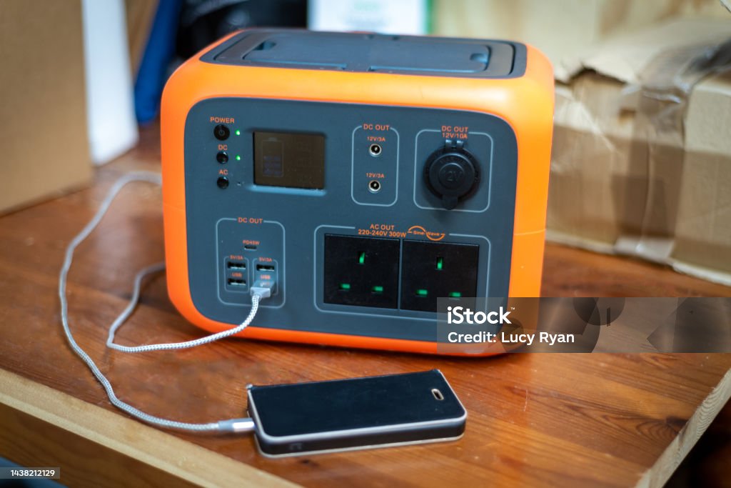 Portable power station solar electricity generator with mobile phone plugged in to charge. Portable power station solar electricity generator with mobile phone plugged in to charge. Wireless charging, lithium battery backup for power outage emergencies or outdoor travel camping. Generator Stock Photo