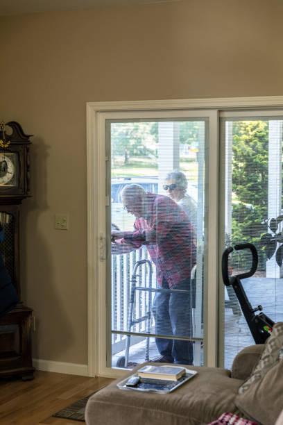 Elderly Senior Adult Man Unlocking Home Sliding Door Arriving back home after visiting a local public nature park with his senior adult woman home caregiver daughter, an elderly senior adult man is ready to sit down to relax in his favorite reclining chair in front of his television. His daughter waits patiently behind him, and his orthopedic walker waits in front of him, as he slowly unlocks the sliding front door of his apartment. walking into glass door stock pictures, royalty-free photos & images