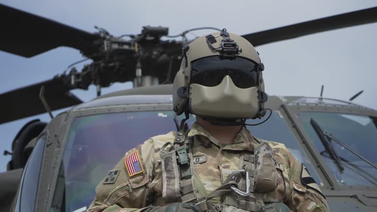 American military helicopter pilot soldier with modern helmet set navigate in front of landed chopper. Air force concept