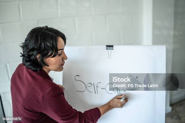 Mid Adult Psychotherapist Woman Writing About Self Care On A Whiteboard Stock Photo - Download Image Now