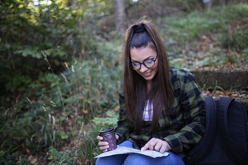A young woman in the forest holding a map and trying to orient herself in the wild
