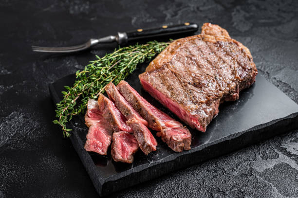 istock Griiled on BBQ sliced Striploin marbled beef meat steak. Black background. Top view 1438231032