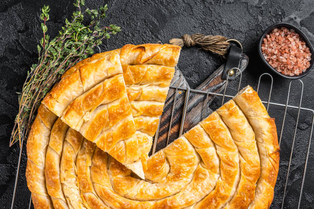 istock Turkish Tepsi Boregi, Round Borek cheese pie on kitchen board. Black background. Top view 1438234740