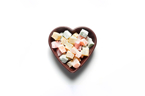 Colorful Turkish delights in a heart-shaped bowl. On a white background.
