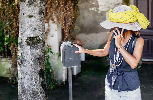 A hispanic woman opens her mail box to find her prescription refilled from her pharmacy sent to her by mail.