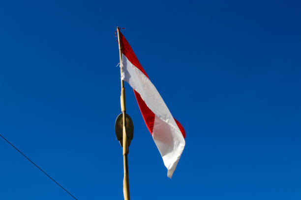 Indonesia flag on a bamboo pole waving in the wind against clear blue sky in the morning.
