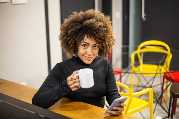 istock Black woman using cellphone and drinking coffee in office break area 1438254163
