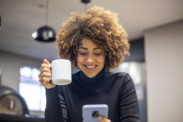 istock Black woman using cellphone and drinking coffee in office break area 1438254170