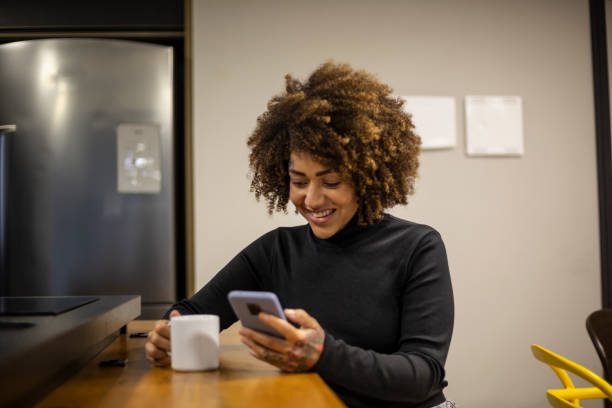 istock Black woman using cellphone and drinking coffee in office break area 1438254215