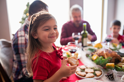 Cute little girl on family gathering eating a Christmas cookie on the table.