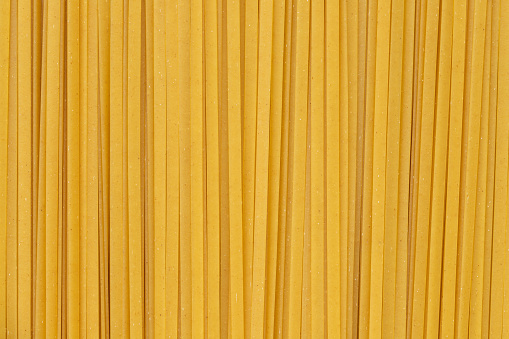 Uncooked dry durum fettuccine pasta. Closeup of raw spaghetti. Full frame of noodles. Food background.