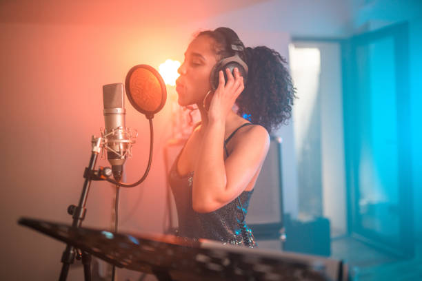 Young Hispanic beautiful female singer singing and recording songs in recording studio. Waist-up, eyes closed.