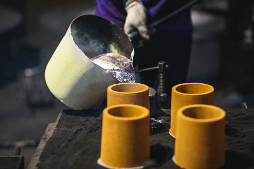 Blue collar worker pouring melted aluminium into molds. He is wearing protective gear and a uniform.