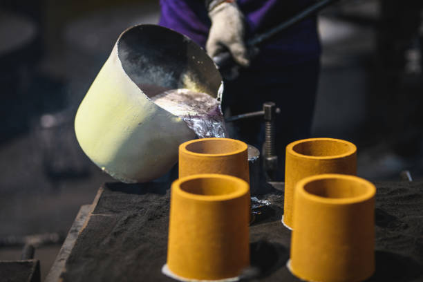 Aluminium Casting And Foundry. Heavy Duty Worker Pouring Liquified Metal Into A Cast Blue collar worker pouring melted aluminium into molds. He is wearing protective gear and a uniform. molten silver stock pictures, royalty-free photos & images