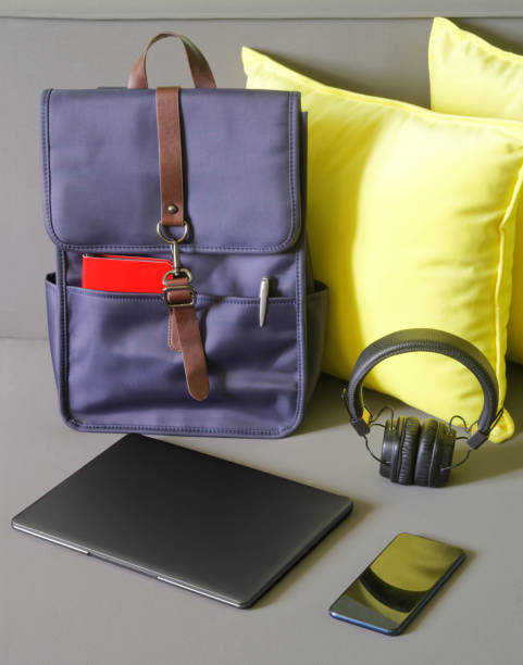 istock Modern trendy urban backpack for a laptop with a notebook and pen stands on a soft sofa next to pillows, a laptop, a smartphone and headphones. Preparing for travel or trip with gadgets. 1438270777