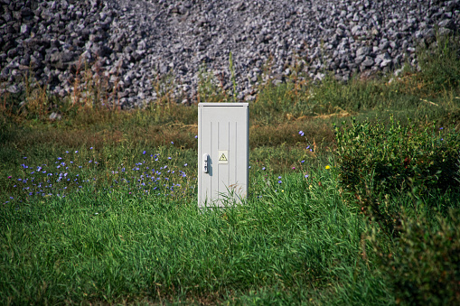 Small gray transformer cabin among green grass, wild flowers and gray stones. Daylight