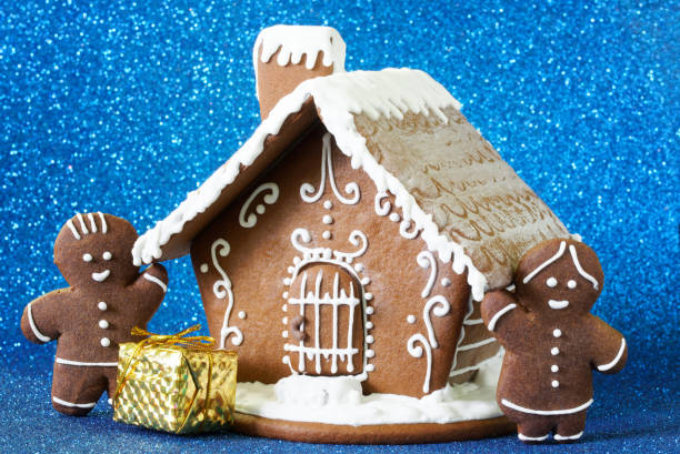 A gingerbread house, a gift and two gingerbread men on a sparkling blue background. An example of decorating a Christmas and New Year's interior. Design blank for the winter holidays. Close-up