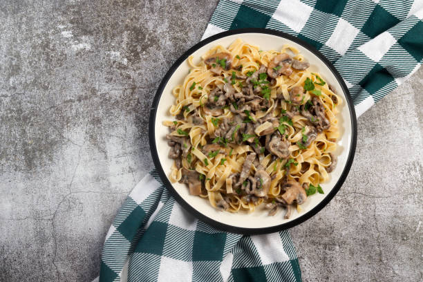 istock Homemade Beef Stroganoff Pasta with herbs on a white round plate on a dark grey background. Top view, flat lay 1438272748