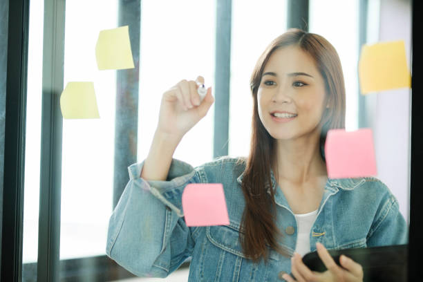 istock Young female student writing study plans on post-its on glass wall. 1438278103