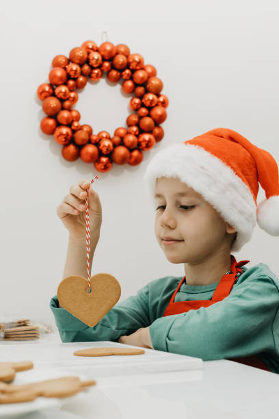 istock A cute boy in a Santa hat holds ginger cookies on a rope while sitting in the kitchen. 1438278948