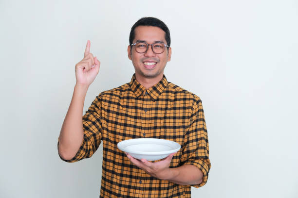 istock Adult Asian man smiling and pointing finger up while holding empty dinner plate 1438281343