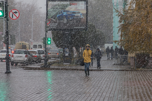 Uralsk, Kazakhstan (Qazaqstan), 29.10.2015 - Autumn snowfall and people in the city. People in the city in a heavy snowfall. Snow with rain and pedestrians. Girl in a yellow jacket in heavy snow and wind. Bad weather. Wet snow