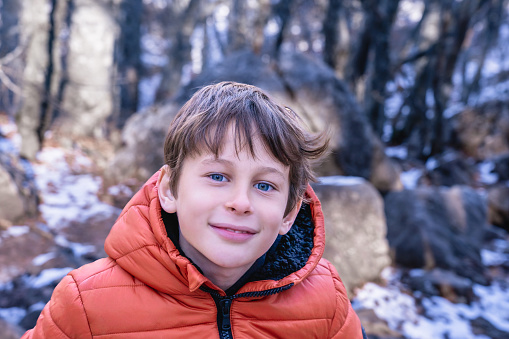 Portrait of a boy (8 years old, white, Caucasian) against a blurred background of a winter mountain forest