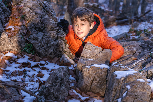 Portrait of a boy (8 years old, white, Caucasian) sanctified by the rays of the sun hiding behind a stone in the mountains in the winter forest during a break between games
