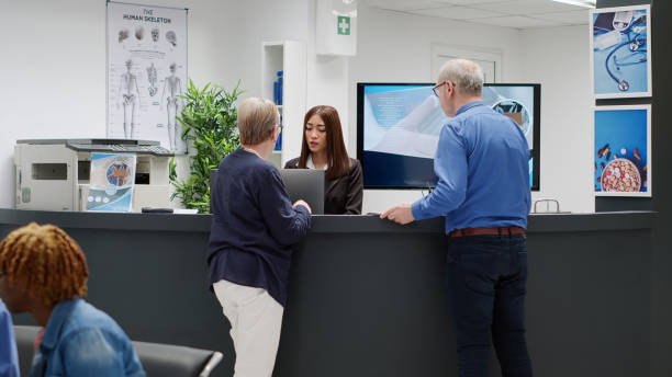 istock Senior people talking to receptionist at hospital reception desk 1438300085