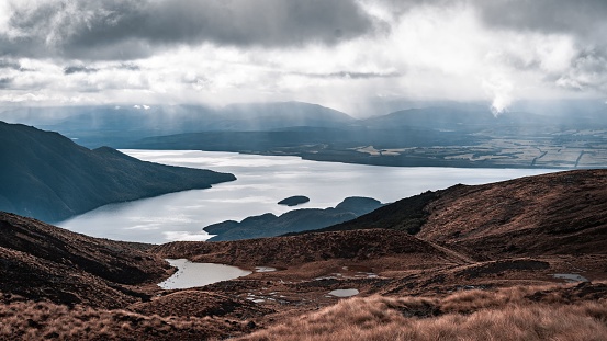 A scenic shot of a lake surrounded by mountains and valleys under a cloudy sky with a heavenly effect