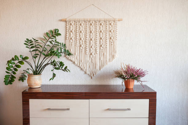 Handmade macrame. 100% cotton wall decoration with wooden stick hanging on a white wall.  Female hobby.  ECO friendly modern knitting DIY natural decoration concept in the interior stock photo