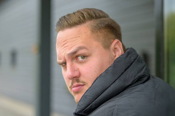 Young man looking over his shoulder Young man showing total disbelief and scepticism as he raises an eyebrow at the camera looking over his shoulder skeptical look stock pictures, royalty-free photos & images