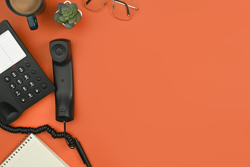 Above view of telephone, notepad, coffee up and eyeglasses on orange background. Flat lay, top view with copy space.